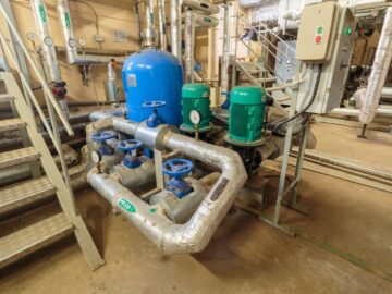 An electric sump pump with a monitor and blue and green tanks in a basement next to a metal staircase.