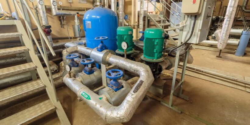 An electric sump pump with a monitor and blue and green tanks in a basement next to a metal staircase.