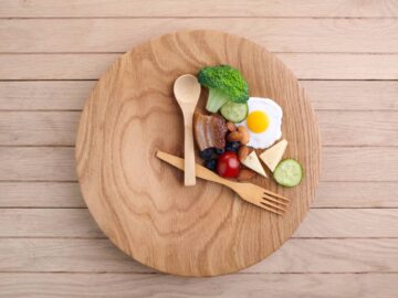 A wooden spoon and fork sit on a plate like hands on a clock face. Food covers the top right third of the plate.