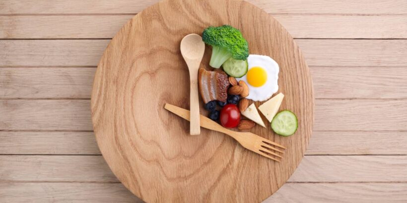 A wooden spoon and fork sit on a plate like hands on a clock face. Food covers the top right third of the plate.