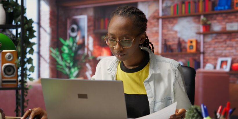 A young person sitting a desk in their at-home remote workspace. They are intently using a silver laptop.