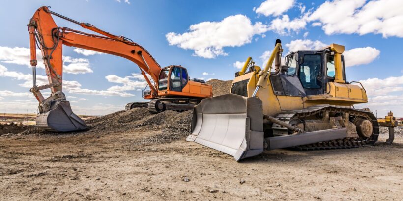 An orange excavator and a yellow bulldozer are positioned on a hilly, dirt-covered jobsite. A blue sky fills the background.