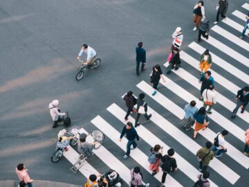 An aerial view of a large group of people using a crosswalk in a city. Several people crossing are on bicycles.