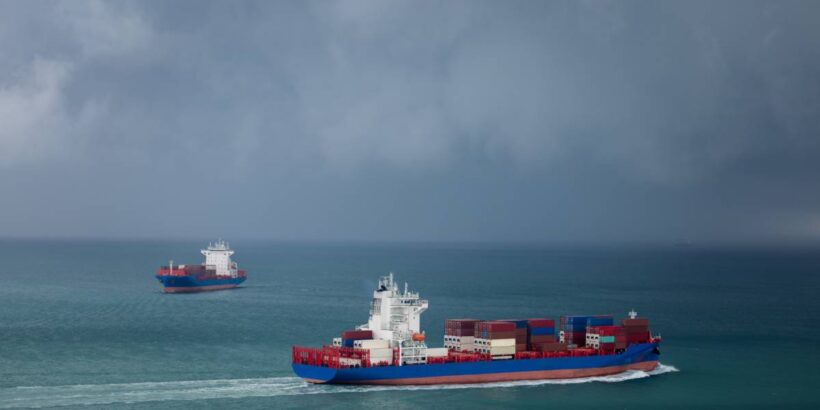 Two cargo container ships sailing past each other in the open ocean. The sky is filled with dark, gloomy clouds.